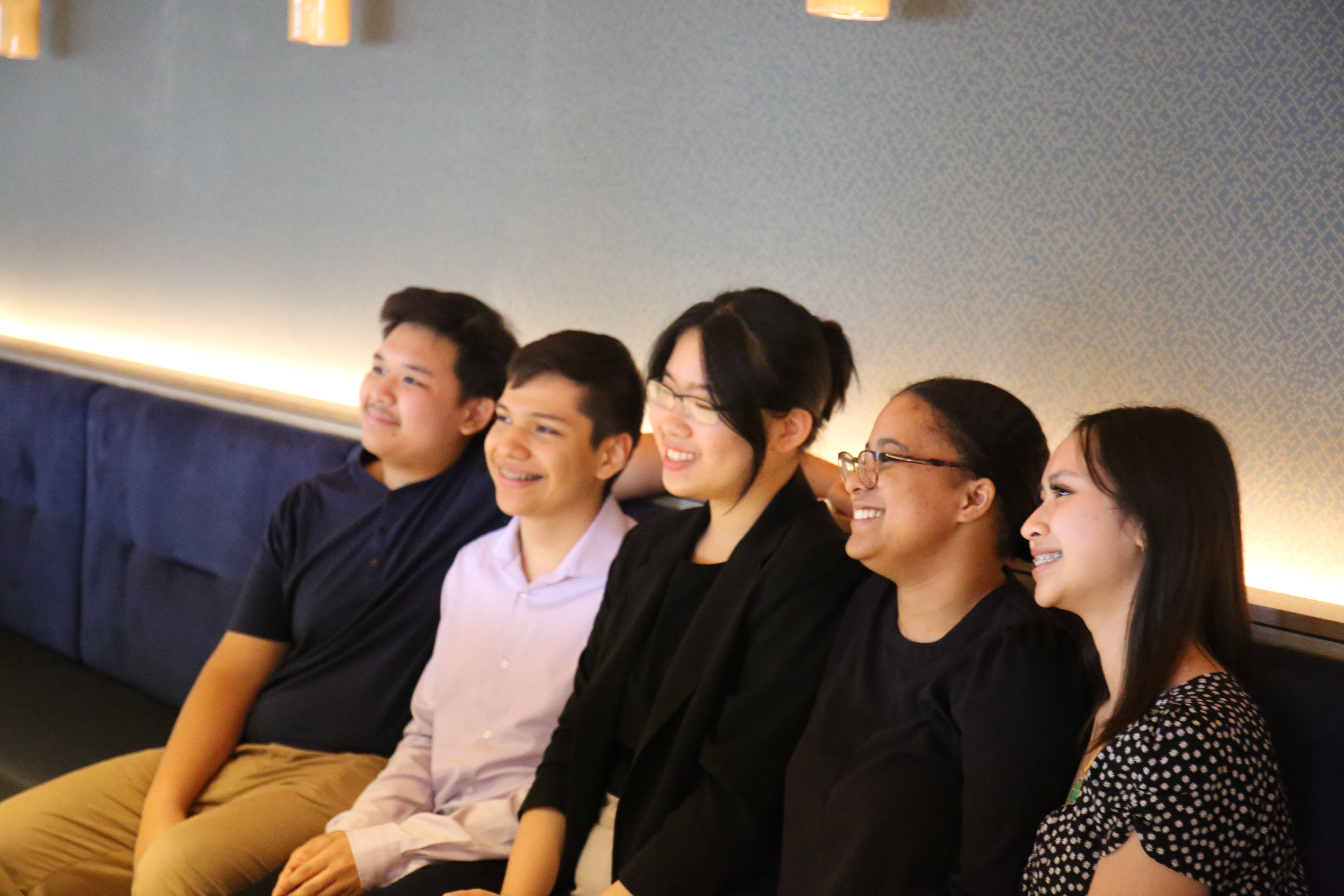 Five people, part of John Hancock’s MLK Scholars program, sit on a bench, smiling and facing forward.