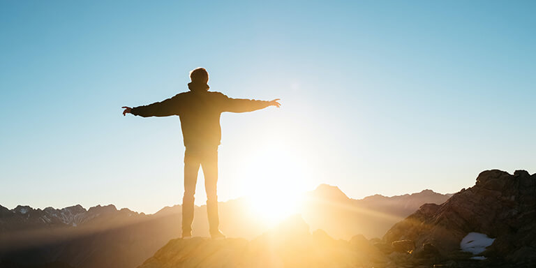 Man standing on the top of a mountain arms raised out and greeting the sunrise 