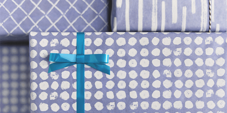 Close up of a present wrapped in purple polka dot wrapping paper with a blue bow